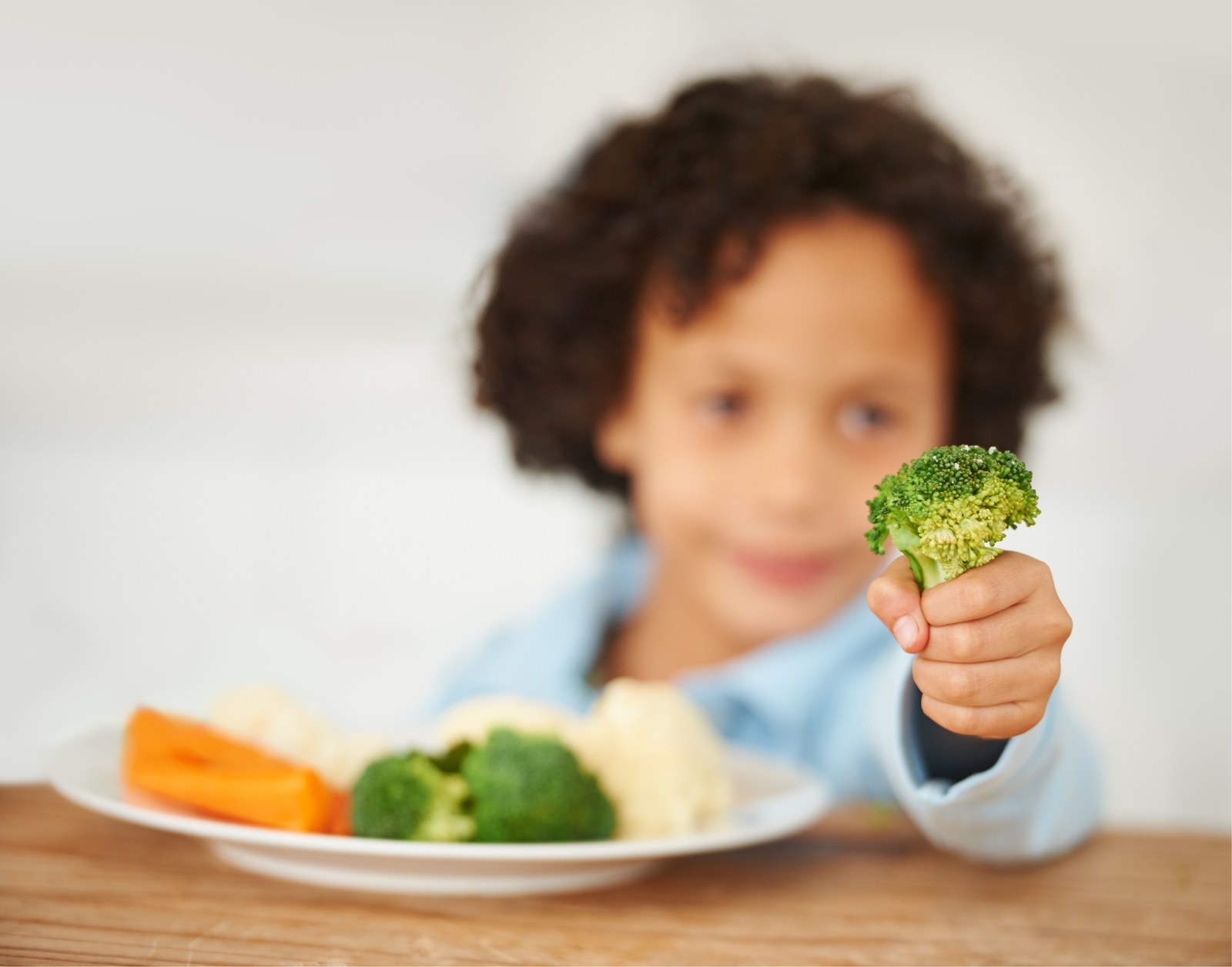 Enfant présentant fièrement un brocoli devant une assiette de légumes